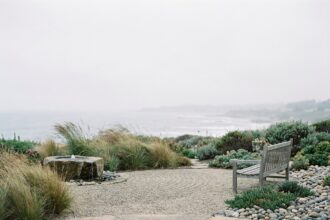 Vue panoramique d'un jardin zen en bord de mer avec graviers, graminées, fontaine en pierre et banc en bois brut